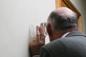 壁に耳を当て隣りの部屋を盗聴する老人男性