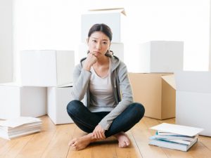 ダンボールに囲まれて座り、考え事をする女性
