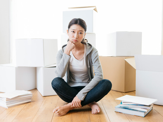 ダンボールに囲まれて座り、考え事をする女性